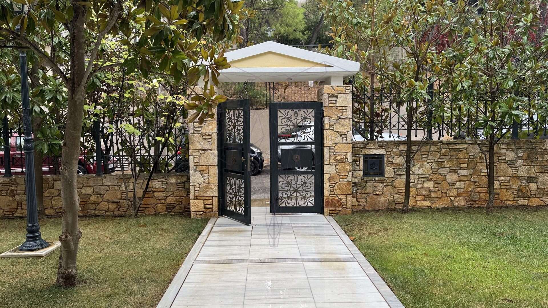 Σιδερένια αυλόπορτα σε πέτρινο φράχτη με δέντρα